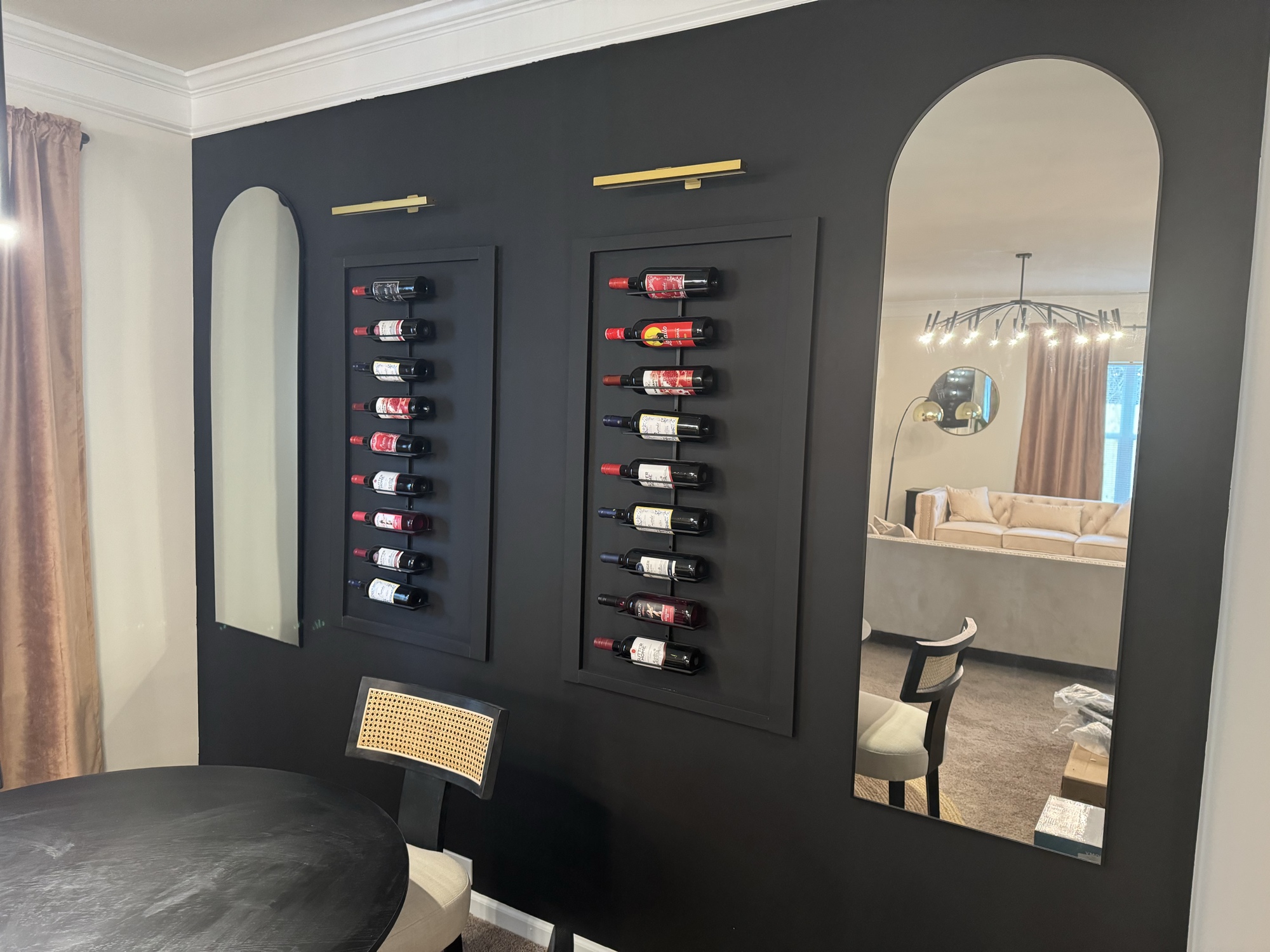 Dramatic black dining room wall with wine racks, arch mirrors and brass sconces