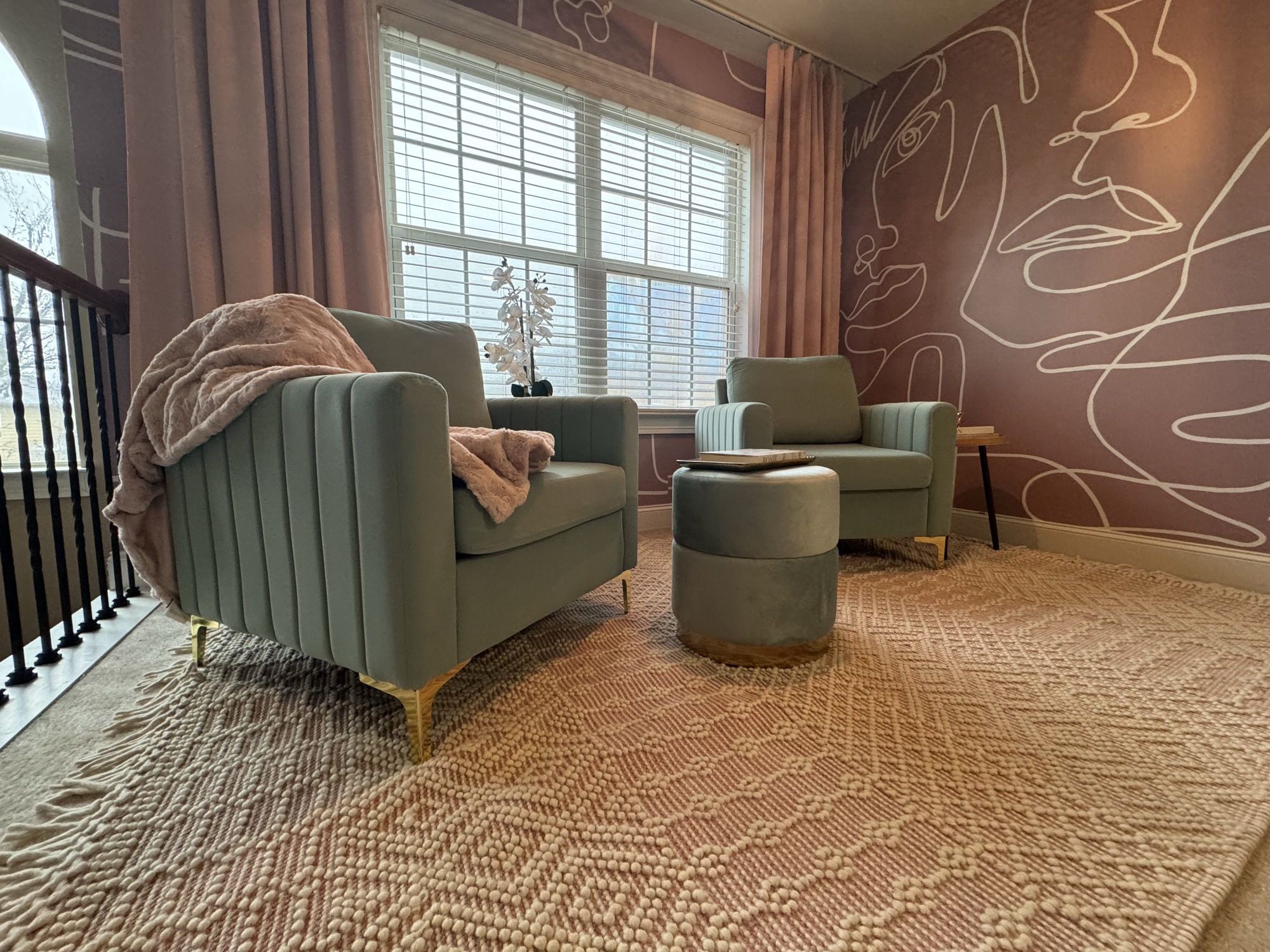 Mauve sitting room with velvet channel-back chairs and abstract face mural