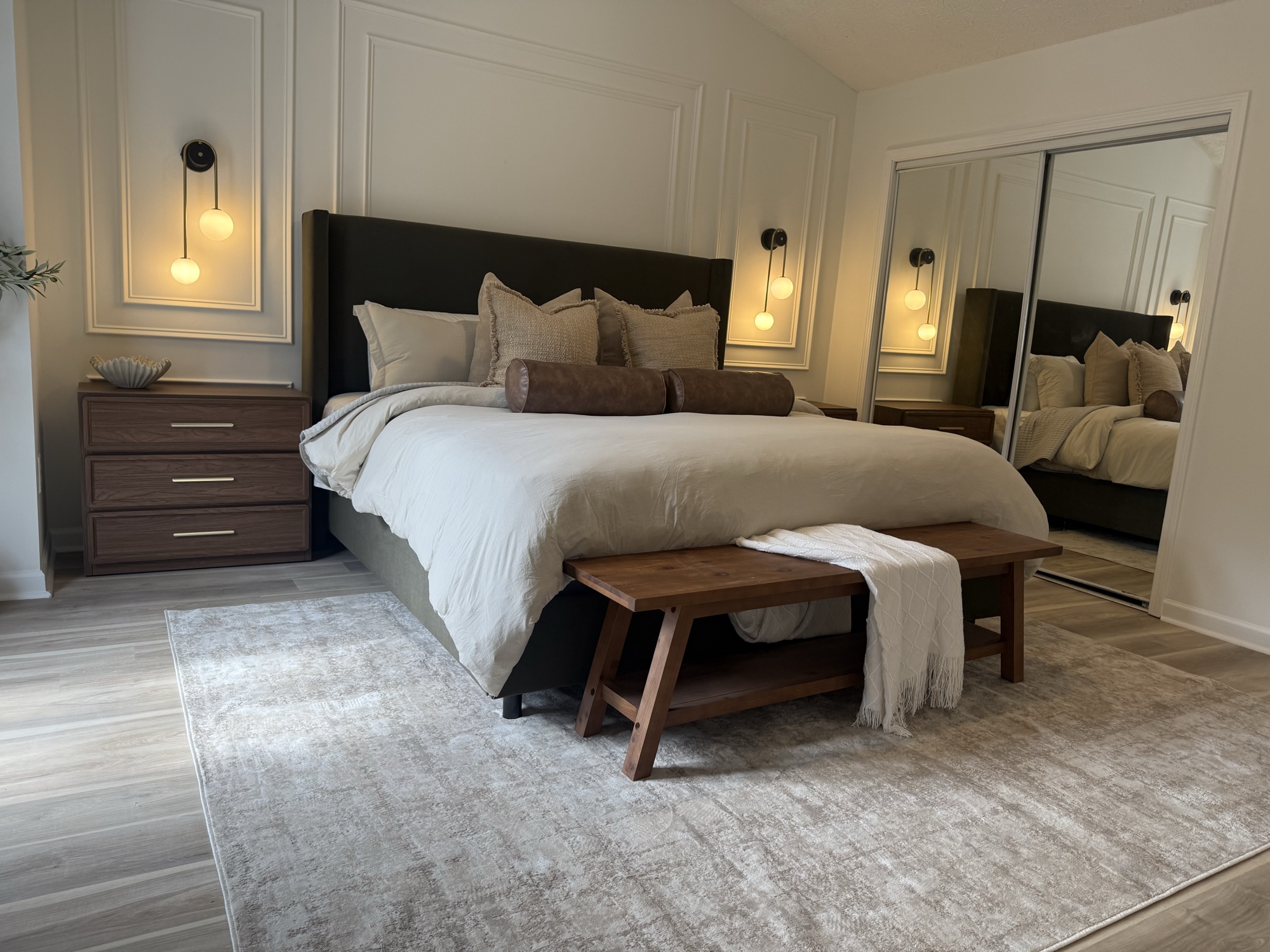 Serene master bedroom with dark wingback headboard, globe sconces and wood bench